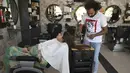 Dalam gambar pada 8 April 2021, tukang cukur Pakistan Ali Abbas menggunakan pecahan kaca untuk memotong rambut seorang pelanggan di tokonya di Lahore. Berharap membuktikan kemampuannya dalam persaingan, Ali Abbas mengandalkan berbagai alat yang tidak biasa untuk melatih keahliannya. (Arif ALI/AFP)