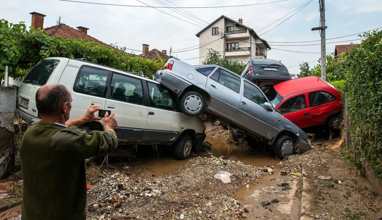 Warga mengambil gambar mobil yang rusak akibat banjir bandang di Ibu Kota Skopje, Makedonia, Minggu (7/8). Pemerintah menyatakan keadaan darurat sehari setelah setidaknya 21 orang tewas dalam banjir bandang yang disebabkan badai. (Robert ATANASOVSKI/AFP)