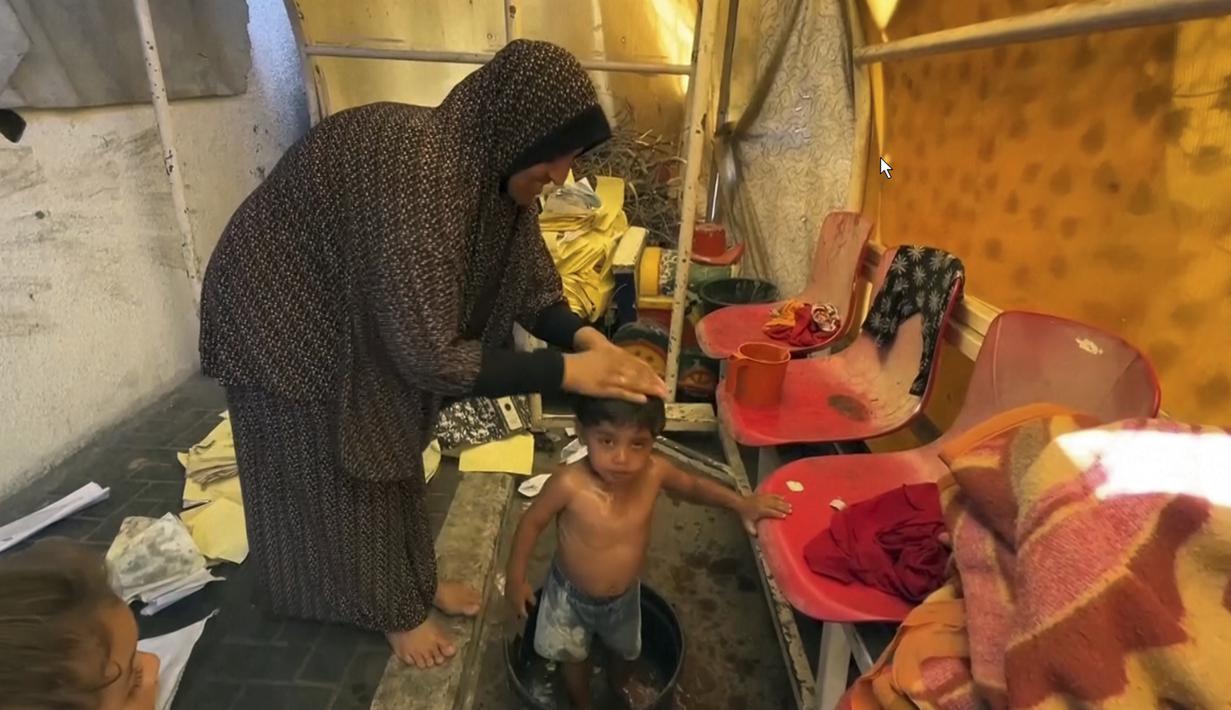 Di bawah bangku tertutup tempat para pemain biasa duduk, Um Bashar memandikan seorang balita yang berdiri di bak plastik. (AP Photo)