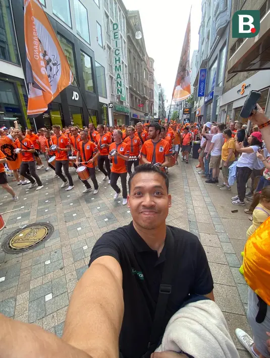 Jurnalis Bola.com, Gerendo Pradigdo di depan grup musik bernama Almondegas yang membimbing para penggemar Belanda untuk bergerak bersama-sama menuju tempat nonton bareng laga semifinal Euro 2024 antara Belanda menghadapi Inggris, Rabu (10/7/2024) dengan alunan musik yang membangkitkan semangat. (Bola.com/Gerendo Pradigdo)