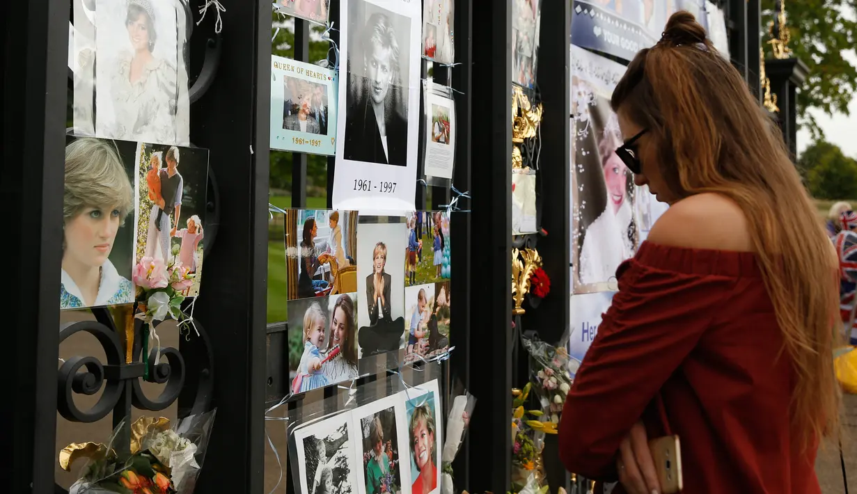 Seorang turis wanita mengamati memorabilia Putri Diana yang diletakkan di luar Istana Kensington, London, Selasa (29/8). Bunga, foto hingga lilin diletakkan di luar Istana untuk mengenang 20 tahun kematian Putri Diana. (AP Photo/Alastair Grant)