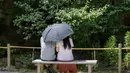 Sepasang kekasih duduk menggunakan payung agar terhindar dari sinar matahari saat mereka berada di kuil Buddha Meigetsu-in di Kamakura, Tokyo, Jepang, Jumat (11/6/2021).  (AP Photo/Kiichiro Sato)