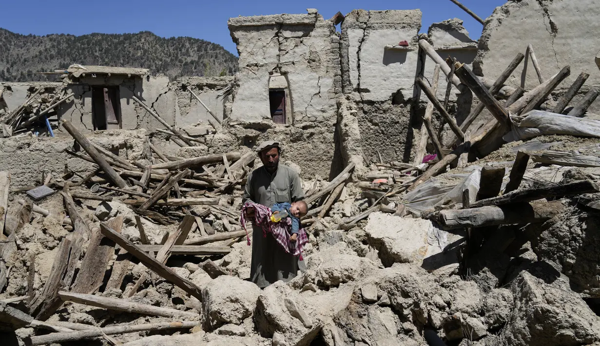 <p>Seorang pria Afghanistan menggendong anaknya di tengah kehancuran setelah gempa bumi di desa Gayan, di provinsi Paktika, Afghanistan, Jumat, 24 Juni 2022. Gempa bumi dahsyat mengguncang Afghanistan pada Rabu 22 Juni 2022 dini hari, kekuatannya dilaporkan mencapai magnitudo 6,1. (AP Photo/Ebrahim Nooroozi)</p>