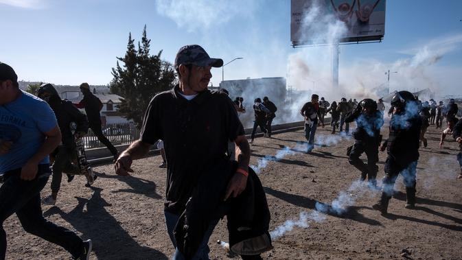 Imigran menghindari gas air mata di dekat pagar pembatas antara Meksiko dan AS di Tijuana, Meksiko (25/11). Walikota Tijuana meminta bantuan PBB untuk menangani sekitar 5.000 migran Amerika Tengah yang telah tiba di kota. (AFP Photo/Guillermo Arias)
