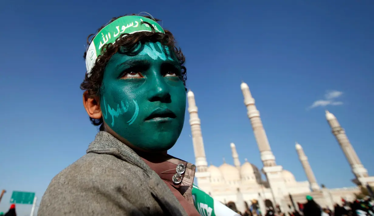 Seorang remaja dengan wajah yang dicat hijau dan bertuliskan kalam Allah, mengikuti peringatan hari kelahiran Nabi Muhammad di Sanaa, Yaman (11/12). (Reuters/Khaled Abdullah)