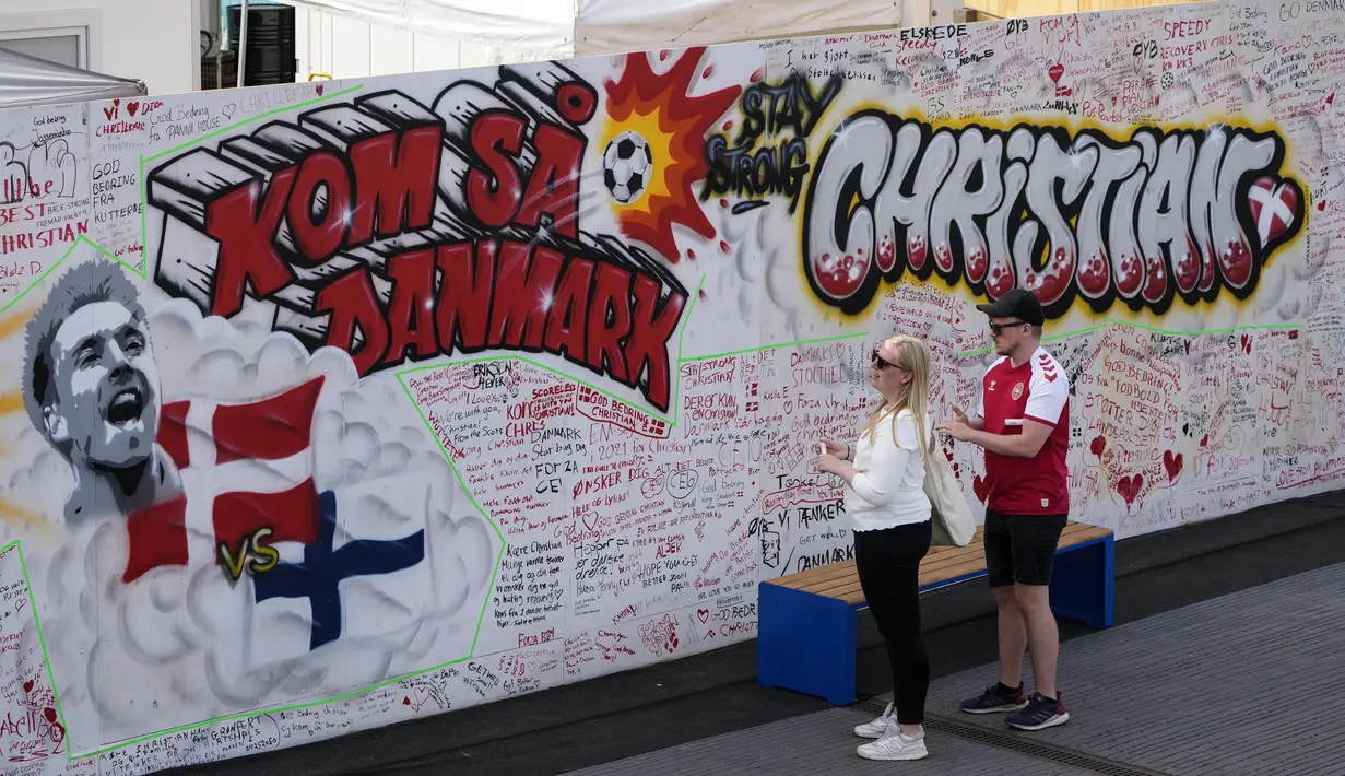 Orang-orang membaca harapan baik pada mural untuk gelandang timnas Denmark Christian Eriksen di dinding fanzone di Kopenhagen, Senin (14/6/2021). Eriksen mengalami serangan jantung dan sempat tak sadarkan diri saat memperkuat timnas Denmark vs Finlandia di Euro 2020. (AP Photo/Martin Meissner)