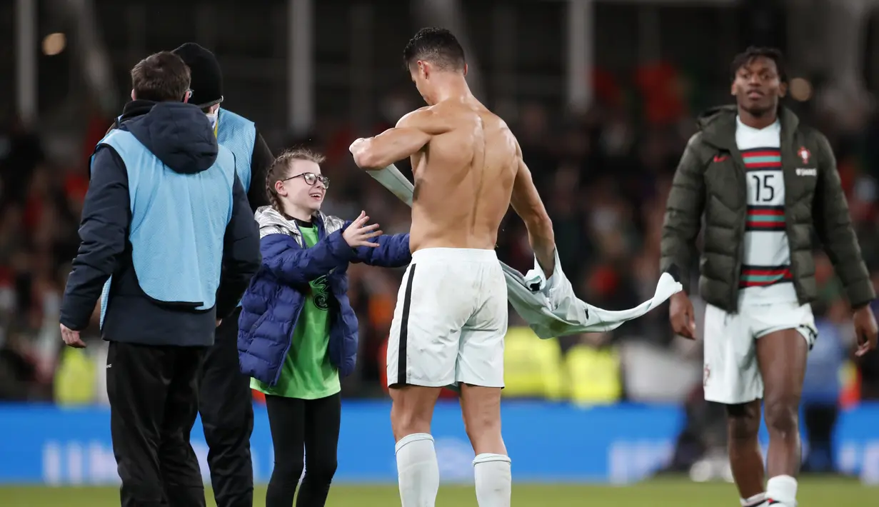 Penyerang Portugal Cristiano Ronaldo memberikan jerseynya untuk fans cilik Irlandia pada akhir laga Grup A Kualifikasi Piala Dunia 2022 Zona Eropa di Stadion Aviva, Jumat (12/11/2021) dinihari. Ronaldo memeluk sang bocah, lalu memberikan jersey tandang Portugal yang dia kenakan. (AP/Peter Morrison)