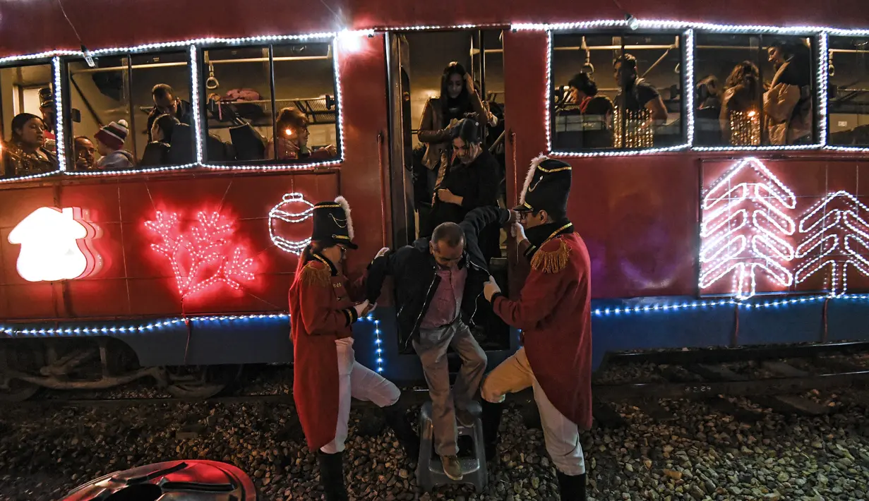 Petugas membantu penumpang turun dari kereta wisata yang dihiasi lampu Natal di Bogota (20/12/2019). Meyambut Hari Natal, kereta wisata di Kolombia membuat cara unik dengan memasangkan lampu warna-warni agar menjadi daya tarik penumpang. (AFP Photo/Juan Barreto)