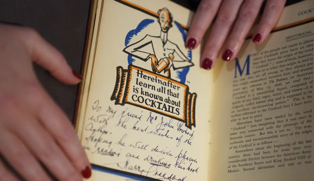 Seorang asisten galeri menunjukkan Savoy Cocktail Book, Harry Craddock (1876 - 1963), diperkirakan antara £1.500 - £2000, selama kunjungan foto untuk sorotan dari Penjualan Minggu Klasik yang akan datang, di Christies, London (3/12/2021). (Kirsty O'Connor/PA via AP)