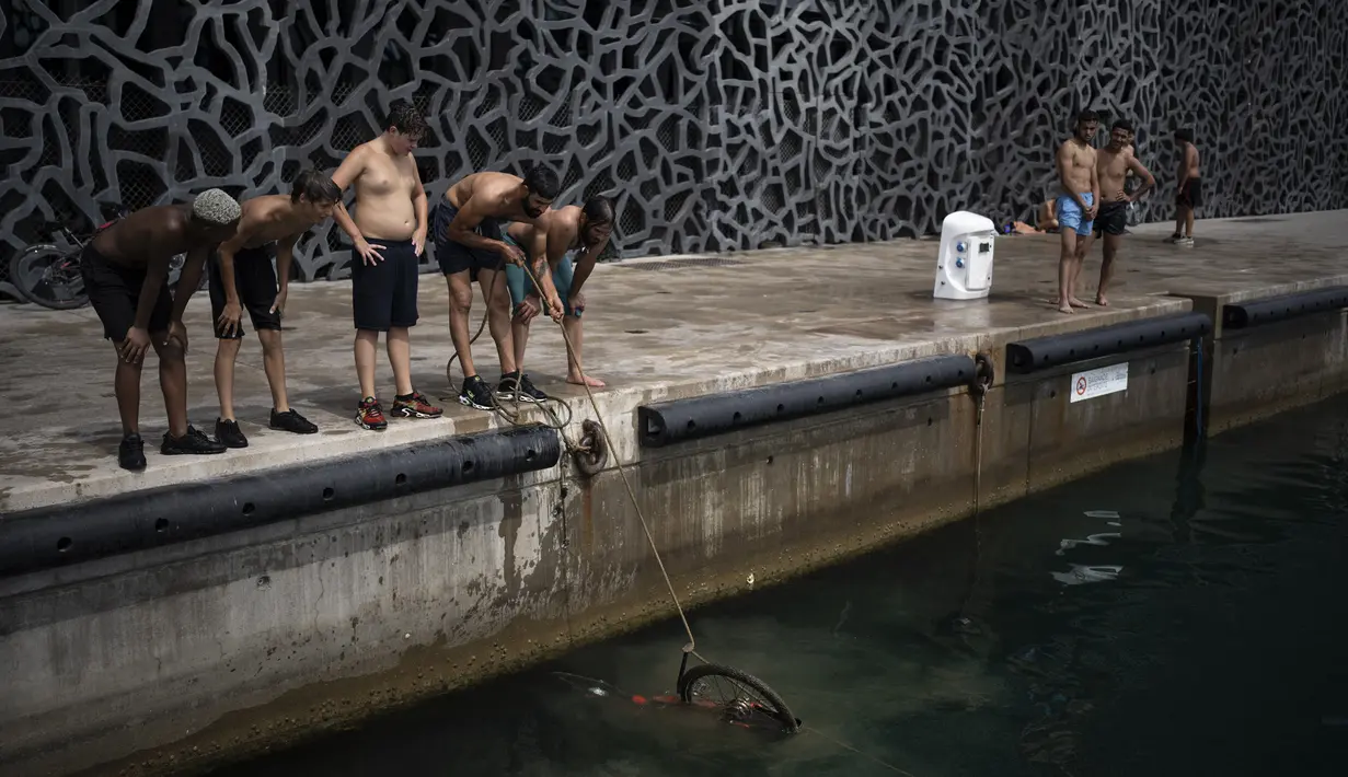 Warga menarik sepeda keluar dari pelabuhan saat gelombang panas di Marseille, Prancis, 15 Juni 2022. (AP Photo/Daniel Cole)