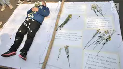 Mahasiswa menaburkan bunga di atas jenazah saat menggelar teatrikal di depan Gedung DPR RI, Jakarta, Selasa (1/10/2019). Aksi teatrikal tersebut sebagai bentuk duka cita atas matinya KPK dan tewasnya dua mahasiswa dalam aksi demonstrasi menolak RKUHP. (merdeka.com/Iqbal S Nugroho)