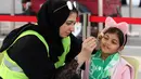 Supoerter wanita Al-Ahli menghias wajah anaknya sebelum menonton timnya melawan Al-Batin  pada laga Saudi Pro League di King Abdullah Sports City, Jeddah, (12/1/2018). Arab Saudi untuk pertama kalinya mengizinkan wanita menonton di stadion. (AFP/STRINGER)