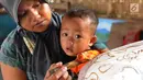 Seorang ibu menggendong anaknya sambil membuat batik tulis di Kampung Batik Puswasedar kawasan Geopark Ciletuh, Sukabumi, Jawa Barat, Sabtu (22/9). Motif batik digali dari beragam sumber Geopark Ciletuh. (Merdeka.com/Arie Basuki)