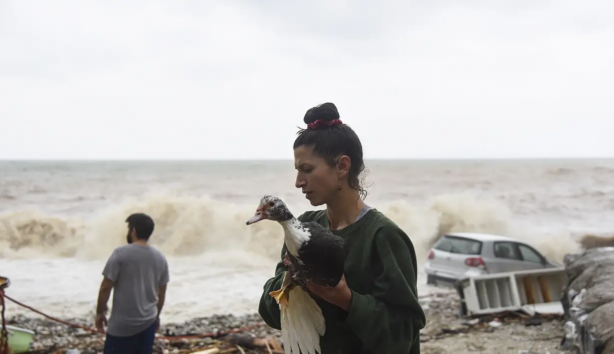 Seorang wanita menyelamatkan seekor burung di pantai setelah badai petir hebat, di desa Paliokastro, di pulau Kreta, Yunani, Sabtu (15/10/2022). Dilaporkan setidaknya satu orang tewas dan lainnya hilang setelah banjir bandang yang parah. (AP Photo/Harry Nakos)