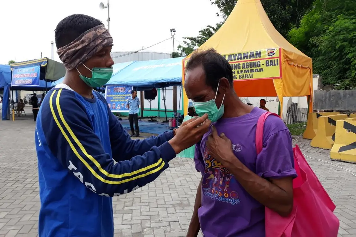 Anggota Taruna Siaga Bencana (Tagana) Provinsi Nusa Tenggara Barat (NTB) membagikan masker kepada para penyintas asal Bali di Pelabuhan Lembar, Lombok Barat, NTB. (Dok: Kemensos)