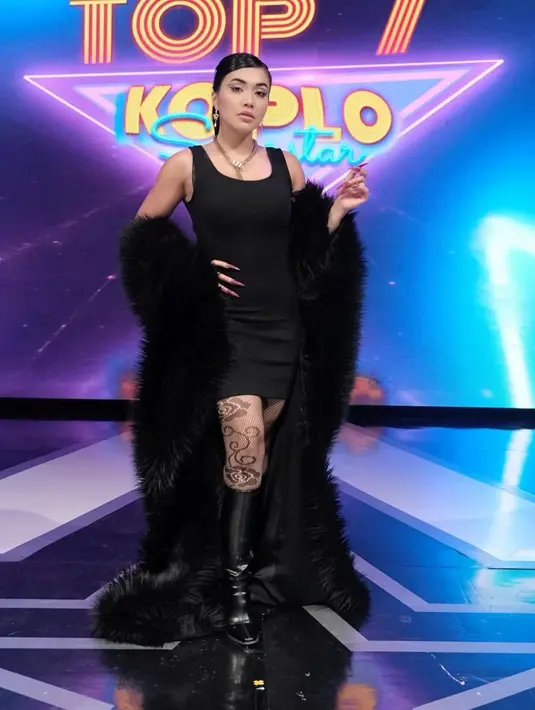 Little black dress yang simple tampil ekstra dengan coat faur fux warna hitam, tight bermotif, dan sepatu boots [@denadaindonesia]