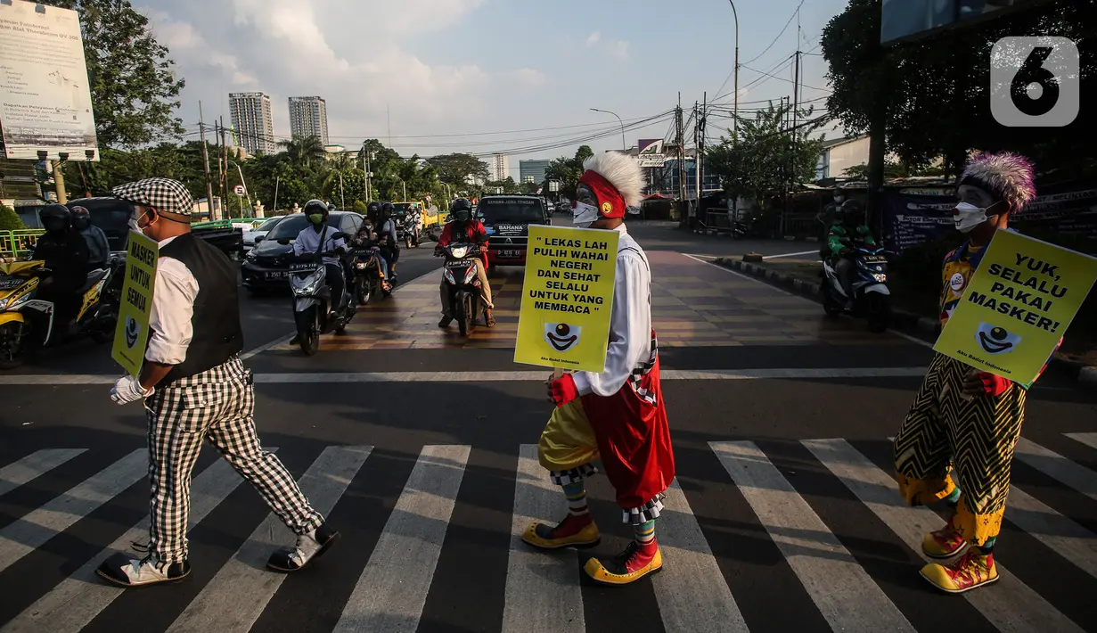 Angggota Komunitas Aku Badut Indonesia (ABI) melakukan aksi kampanye penggunaan di kawasan Cilandak, Jakarta Selatan, Senin (12/7/2021). Selain itu, mereka juga membagi-bagikan masker secara gratis bagi para pengendara motor yang melintas. (Liputan6.com/Johan Tallo)