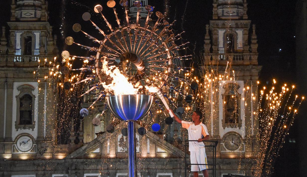Atlet Brasil, Jorge Alberto Gomes, menyalakan obor Olimpiade dengan latar Gereja Candelaria pada pembukaan Olimpiade Rio 2016 di Rio de Janeiro (5/8/2016). (AFP/Mark Ralston)