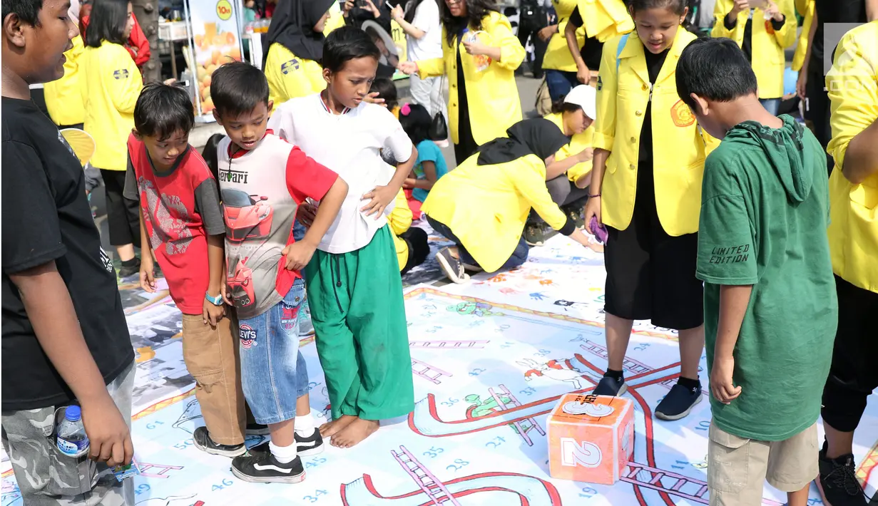 Mahasiswa jurusan Kriminologi Fisip UI mendampingi anak-anak bermain ular tangga saat gelaran Car Free Day di kawasan Bundaran HI, Jakarta, Minggu (18/11). Permainan ini bertujuan mengurangi anak-anak bermain gawai. (Liputan6.com/Helmi Fithriansyah)
