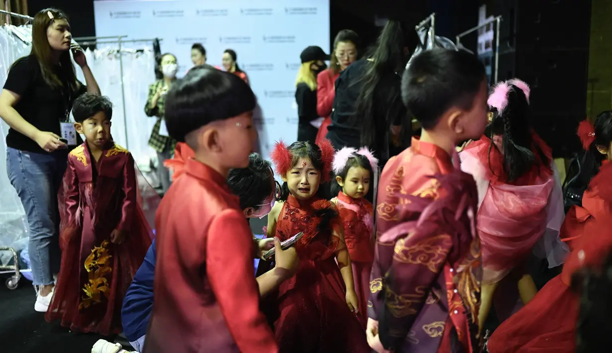 Seorang model cilik (tengah) menangis saat menunggu di belakang panggung sebelum membawakan koleksi Jinshangyuyi karya desainer Wang Cong selama China Fashion Week di Beijing pada Kamis (9/9/2021). Gelaran pekan mode tersebut tetap digelar di tengah pandemi corona covid-19. (Giok GAO / AFP)