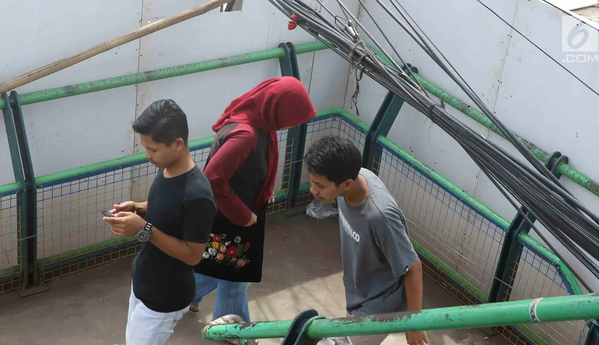 Pejalan kaki melintasi jembatan penyeberangan orang yang terhalang instalasi kabel di Depok, Jawa Barat, Sabtu (8/12). Selain mengganggu kenyamanan, keberadaan instalasi kabel semrawut tersebut membahayakan pejalan kaki. (Liputan6.com/Immanuel Antonius)