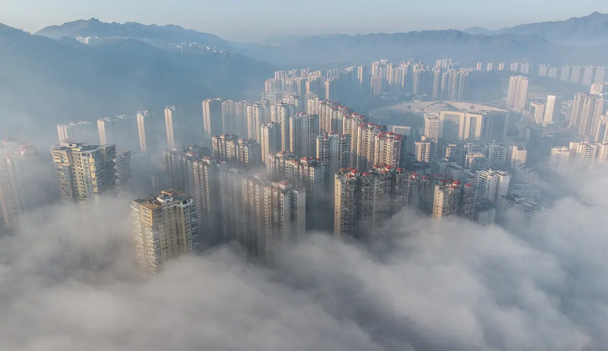 Foto udara ini menunjukkan bangunan yang diselimuti kabut pagi di Bijie, provinsi Guizhou barat daya China (18/11/2021).  Kota ini menerima 1.218 jam sinar matahari yang cerah setiap tahunnya; musim semi lebih cerah dan memiliki suhu siang hari yang lebih hangat daripada musim gugur. (AFP/STR)