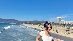 Beby Tsabina berpose dengan latar belakang pantai di California. Beby tampak lebih dewasa memakai mini dress dengan rambut di kuncir. Poni rambutnya 
 yang panjang mempermanis wajahnya yang sudah sempurna. (Instagram/bebytsabina)