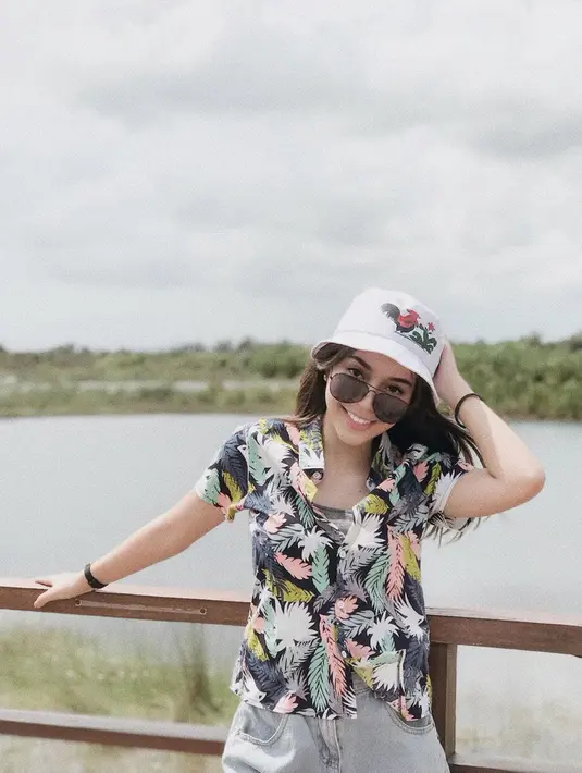 Gadis cantik yang sekarang sudah berusia 19 tahun ini tampak bahagia saat liburan ke Pulau Belitung. Menggunakan kemeja pantai dengan motif warna-warni, penampilannya semakin lengkap dengan kacamata hitam dan topi ikonik bergambar mangkok mie ayam. (Liputan6.com/IG/faynabilalxndr)