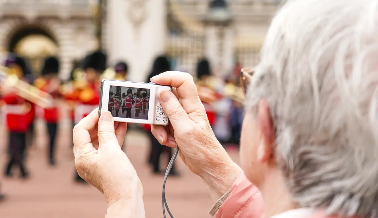 Seseorang mengambil gambar prosesi pergantian penjaga di Istana Buckingham, London, Senin (23/8/2021). Pergantian pasukan jaga yang dilengkapi dengan alat musik lengkap ala marching band tersebut berlangsung untuk pertama kalinya sejak dimulainya pandemi corona Covid-19. (AP Photo/Alberto Pezzali)