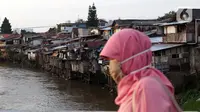 Warga melintas di jembatan berlatar pemukiman di kawasan bantaran Kali Ciliwung, Jakarta, Rabu (10/3/2021). Wagub DKI Jakarta Ahmad Riza Patria mengungkap dua kendala terkait pembebasan lahan untuk normalisasi Sungai Ciliwung sebagai upaya mencegah banjir. (Liputan6.com/Helmi Fithriansyah)