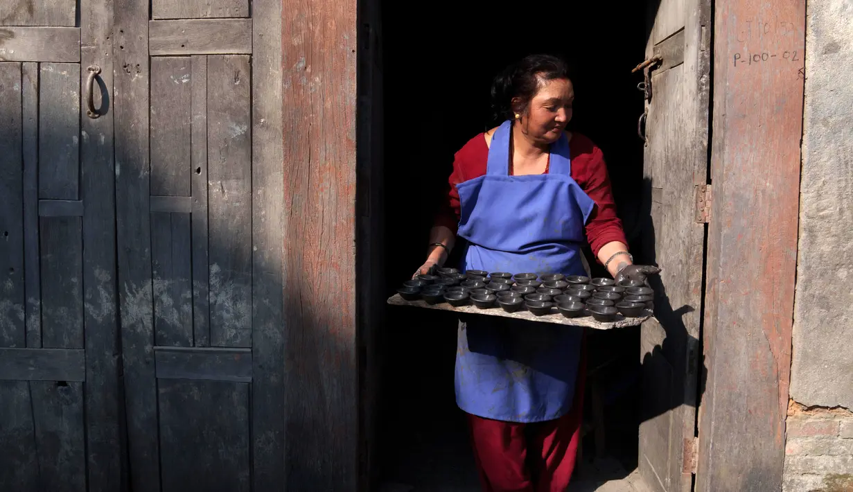 Seorang pembuat tembikar membawa lampu tanah yang dipersiapkan untuk Festival Tihar atau Yama Panchak di Bhaktapur, Nepal, 21 Oktober 2022. Selama festival lima hari yang mirip dengan Festival Diwali di India tersebut, umat Hindu mendekorasi rumah dan tempat ibadah mereka. (AP Photo/Niranjan Shrestha)