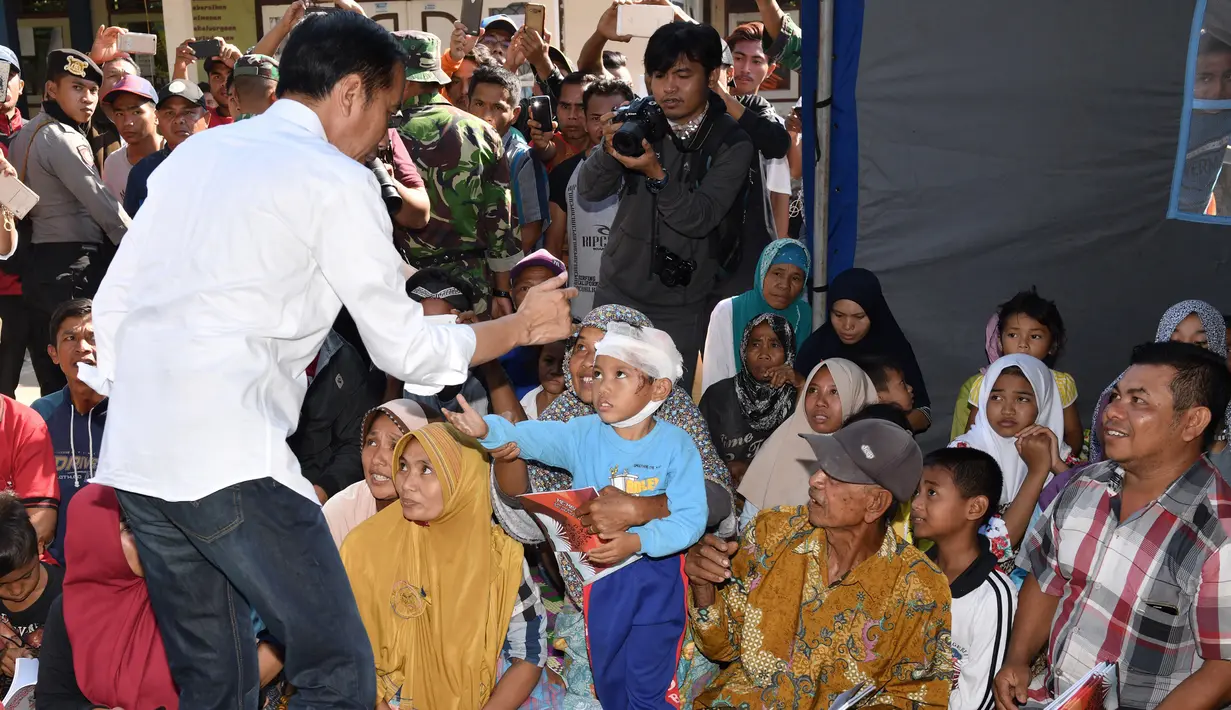 Presiden Joko Widodo atau Jokowi membagikan buku kepada seorang anak saat mengunjungi korban gempa di Desa Madayin, Sambelia, Lombok Timur, NTB, Senin (30/7). (Agus Suparto/Indonesian Presidential Palace/AFP)