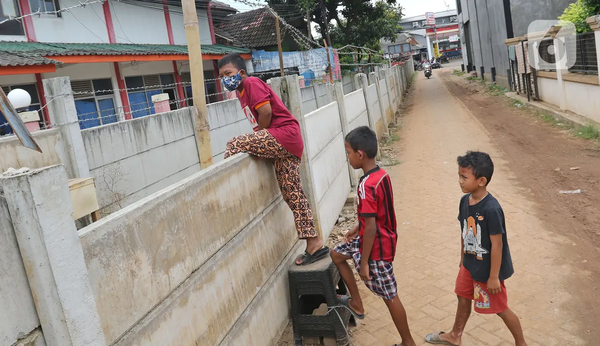Anak-anak memanjat tembok untuk memasuki rumahnya di kawasan Ciledug, Kota Tangerang, Banten, Senin (15/3/2021). Tembok beton sepanjang 300 meter dengan tinggi 2 meter serta dipasang kawat duri itu menutup akses menuju rumah dan tempat usaha milik warga. (Liputan6.com/Herman Zakharia)
