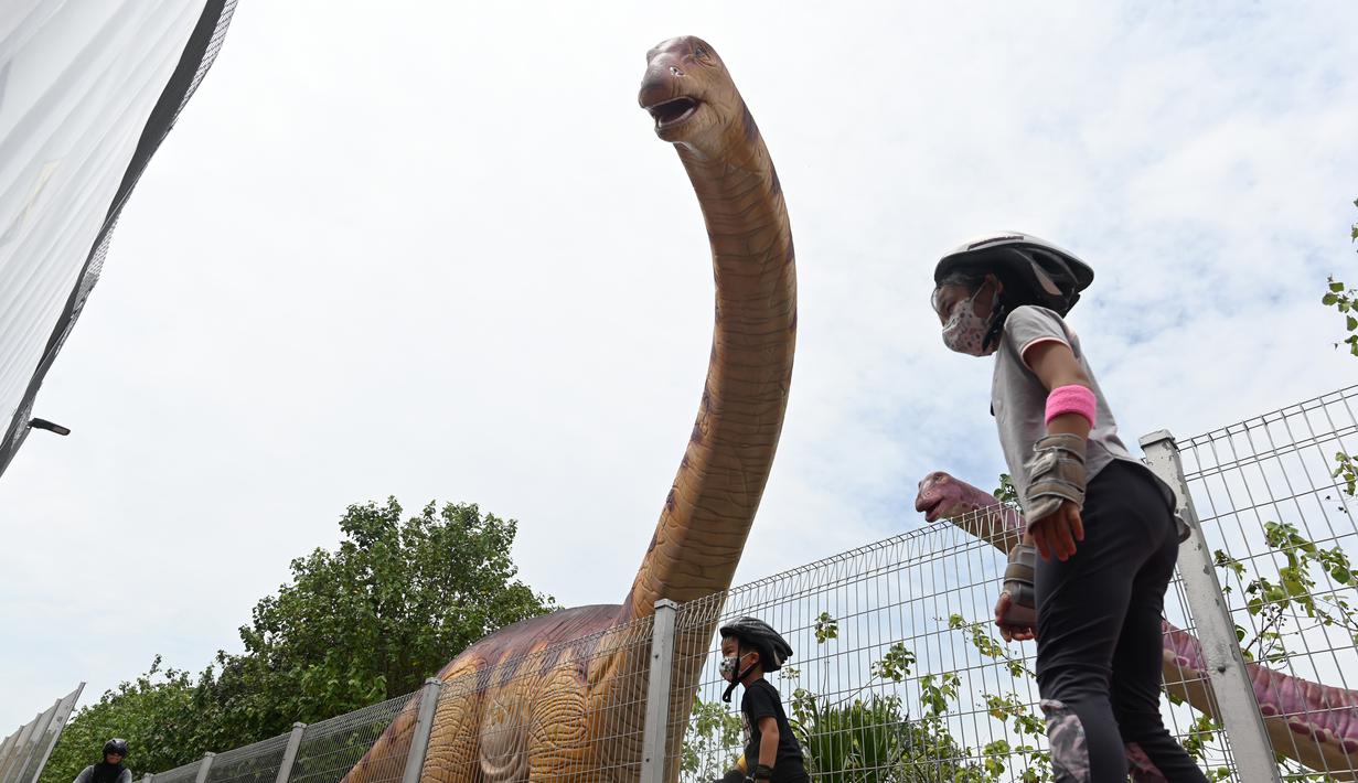 Anak-anak meluncur melewati model dinosaurus seukuran aslinya, Brachiosaurus di sepanjang "Changi Jurassic Mile" jalan santai di Singapura (13/10/2020). (AFP/Roslan Rahman)