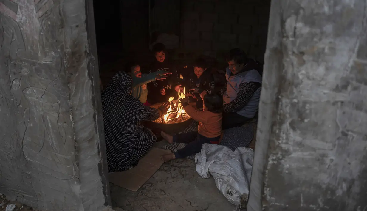 Sebuah keluarga Palestina menghangatkan diri di dekat api saat cuaca dingin di daerah kumuh di pinggiran kamp pengungsi Khan Younis, Jalur Gaza selatan pada Rabu, 19 Januari 2022. (AP Photo/Khalil Hamra)