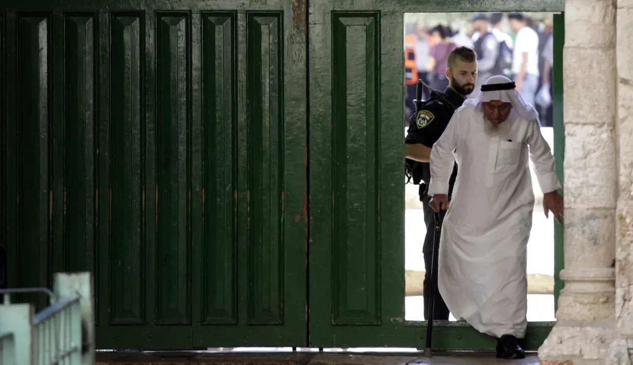 Seorang petugas Israel memberi pengawasan ketat terhadap umat muslim saat berjalan keluar komplek Masjid Al-Aqsa, Yerusalem, Sabtu, (15/7). Penjagaan ini dilakukan demi menjaga ketertiban tempat suci agar tidak terjadi kericuhan lagi. (AP/Mahmoud Illean)