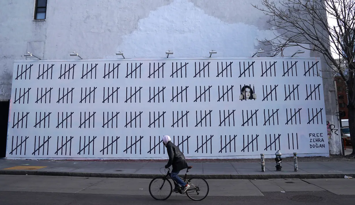 Seorang pengendara sepeda melewati tembok besar yang dimural oleh seniman Banksy di wilayah Manhattan, New York (15/3). Secara keseluruhan mural ini menggambarkan sosok Zehra Dogan yang berada di balik jeruji besi. (AFP Photo/Timothy A. Kliit)