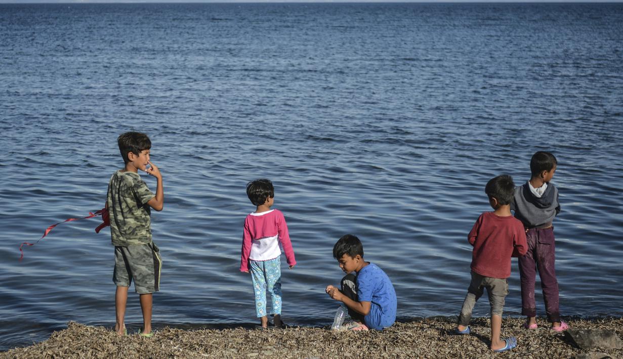 Anak-anak berdiri di tepi laut di kamp pengungsi Kara Tepe, di pulau Lesbos di timur laut Aegean, Yunani (14/10/2020).  Sekitar 7.600 pengungsi dan migran telah menetap di kota tenda baru setelah kebakaran yang menghancurkan kamp pengungsi Moria. (AP Photo/Panagiotis Balaskas)