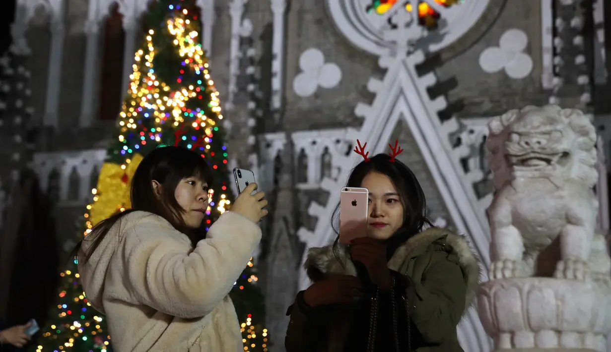 Dua wanita berselfie di depan Gereja Katolik Xishiku saat Malam Natal di Beijing, China (24/12). (AP Photo/Ng Han Guan)