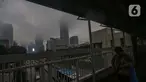 Warga melintas di salah satu Jembatan Penyeberangan Orang (JPO) berlatar suasana gedung bertingkat yang diselimuti kabut di sekitar jalan Jenderal Gatot Subroto, Jakarta, Sabtu (6/7/2024). (Liputan6.com/Angga Yuniar)