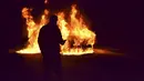 Seorang pria lewat di depan sebuah mobil yang dibakar saat protes terhadap tindakan penguncian yang ketat di Tripoli, Lebanon utara (26/1/2021). Banyak dari penduduk telah kehilangan pendapatan sejak Lebanon memberlakukan lockdown penuh awal bulan ini. (AP/STR)