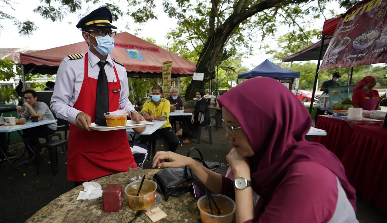 Azrin Mohamad Zawawi menyajikan hidangan kepada pelanggan di warung makannya di Subang Jaya, Malaysia, Rabu (4/11/2020). Kapten Azrin, mantan pilot maskapai Malindo itu bersama 2.200 karyawan lainnya kehilangan pekerjaan usai di-PHK pada akhir Oktober akibat virus corona. (AP Photo/Vincent Thian)
