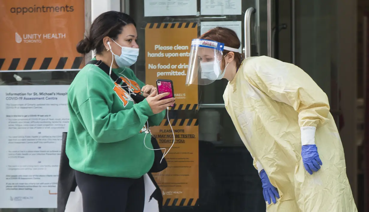 Petugas medis yang mengenakan alat pelindung diri memeriksa informasi janji temu seorang wanita di pusat penilaian COVID-19, Toronto, Kanada, 6 Oktober 2020. Jumlah kasus harian COVID-19 di Kanada terus bertambah. (Xinhua/Zou Zheng)