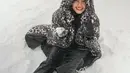 Fuji main salju di tengah badai mengenakan outfit serba hitam. Fuji memadukan turtleneck hitam dengan celana panjang kulit yang juga berwarna hitam, ditumpuk dengan long puffer jacket bercorak totol macan bernuansa hitam. [Foto: Instagram/fuji_an]