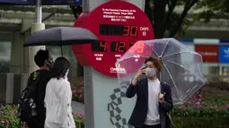 Pejalan kaki berada dekat jam hitung mundur yang menunjukkan 30 hari menuju pembukaan Olimpiade Tokyo 2020 di Tokyo, Rabu (23/6/2021). Olimpiade Tokyo dimulai pada 23 Juli dan penyelenggara mengizinkan penonton lokal menghadiri venue pertandingan dengan kapasitas 50 persen. (AP Photo/Kiichiro Sato)