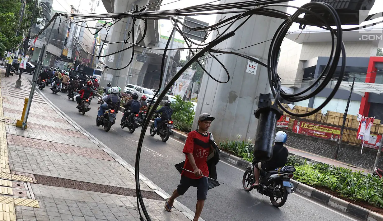 Pejalan kaki melintasi trotoar yang terhalang instalasi kabel di Jalan Kyai Maja, Jakarta, Rabu (10/4). Selain menganggu kenyamanan pejalan kaki, kondisi instalasi kabel yang semrawut tersebut juga berbahaya apabila mengandung aliran listrik. (Liputan6.com/Immanuel Antonius)