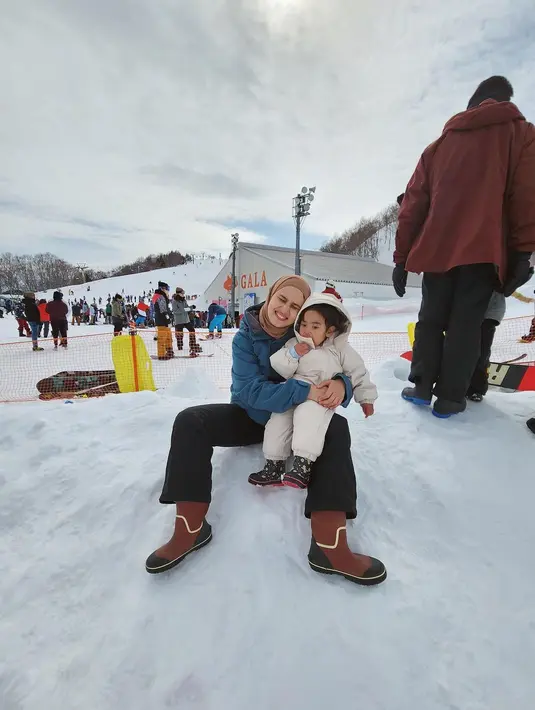 Berpose di tengah salju, Dwi Handayani memeluk sang buah hati dengan gemas. Dwi Handayani mengenakan puffer jacket biru dengan celana panjang hitam, sedangkan sang buah hati mengenakan set puffer jacket yang senada dengan celana panjang berwarna putih gading. Foto: Instagram.