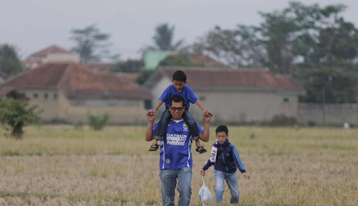 Seorang ayah menggendong anaknya saat melintasi sawah kering menuju Stadion Si Jalak Harupat, Bandung. (Bola.com/Vitalis Yogi Trisna)