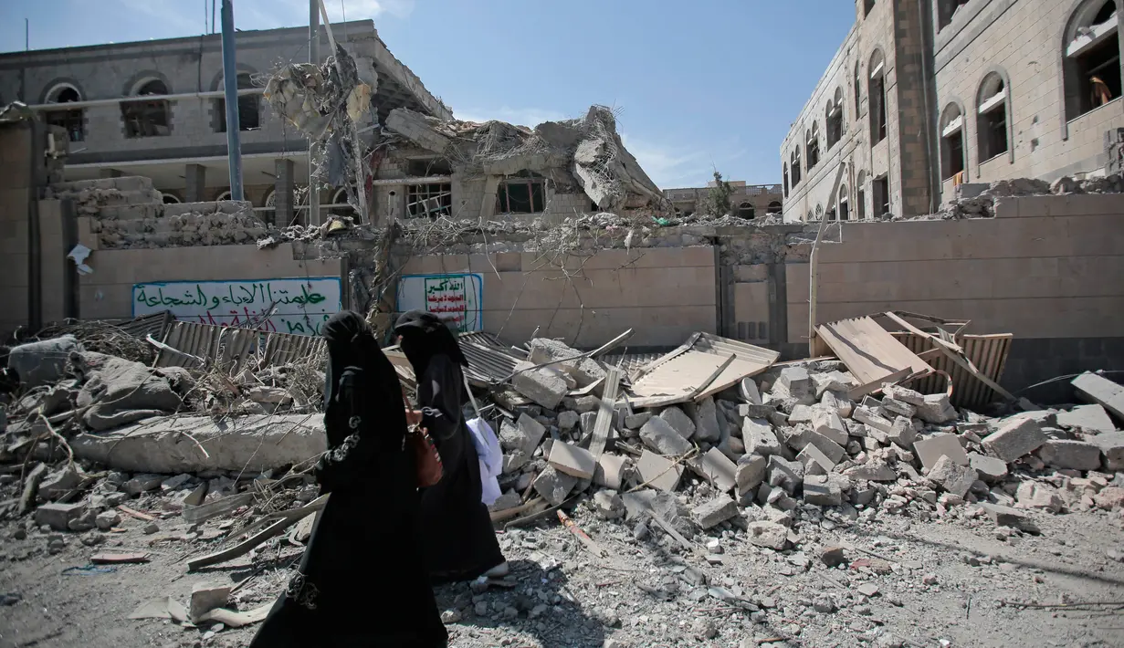 Dua orang wanita berjalan melewati puing-puing gedung yang runtuh di kompleks kepresidenan, di Sanaa, Yaman (7/5). Jet tempur koalisi yang dipimpin Arab Saudi melancarkan serangan udara ke istana kepresidenan Yaman. (AP Photo/Hani Mohammed)