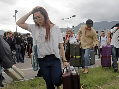 Penumpang berjalan kaki ke bandara ketika pemrotes pro-demokrasi memblokir jalan di luar bandara di Hong Kong (1/9/2019). Demonstran pro-demokrasi penentang RUU Ekstradisi kembali menjadikan bandara sebagai tempat aksi demo. (AP Photo/Kin Cheung)